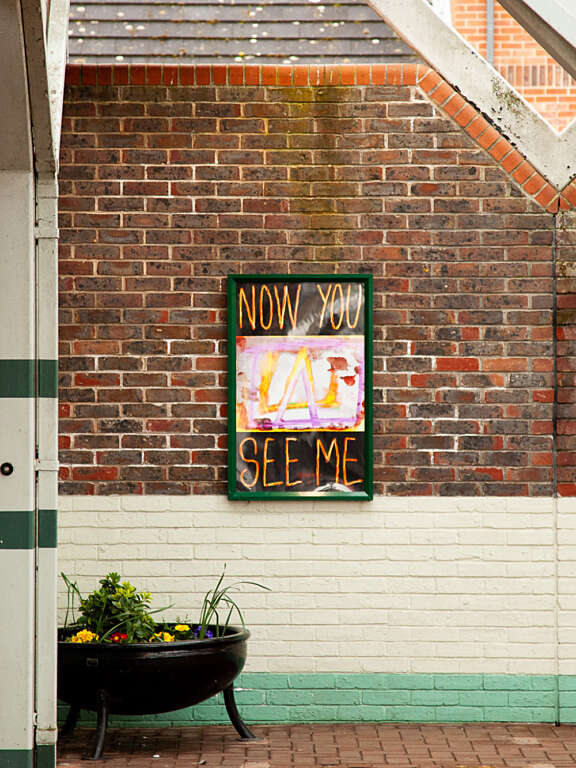 Young person's artwork displayed on the wall of a local train station, with graphic text that says "now you see me"