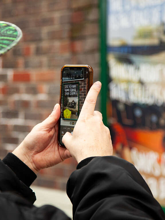 A man taking a photo of a young person's artwork in a local train station using their smart phone