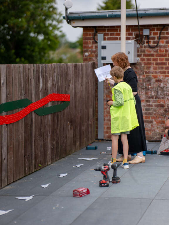 young boy and older woman looking at a piece of paper in front of a half done art installation, tools nearby