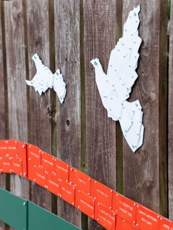 3d installation of white doves and orange and green lines made up of plastic train tickets