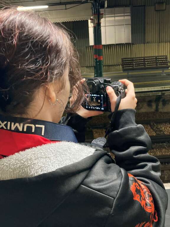 a young girl taking a photo of a train station platform