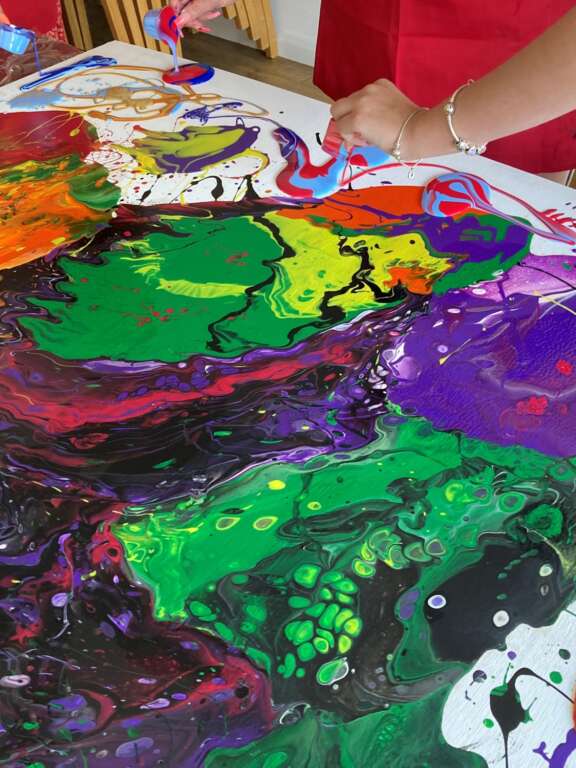 Young people pouring colourful paint onto surface to create artwork