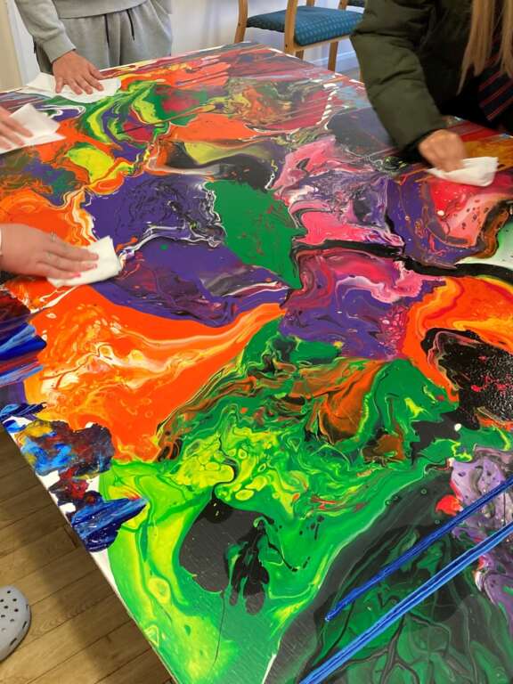 Young people wiping the surface of a colourful artwork of poured paint