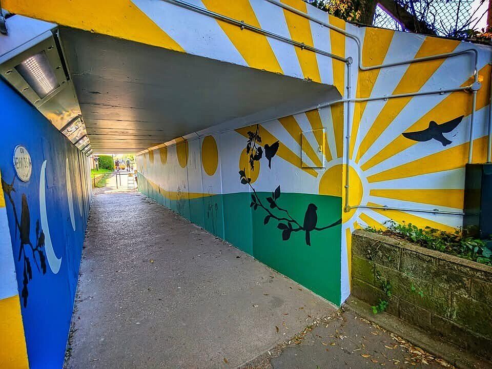 Bright ray of sun mural on entrance to and inside of a subway tunnel with darker design of moons on the opposite side