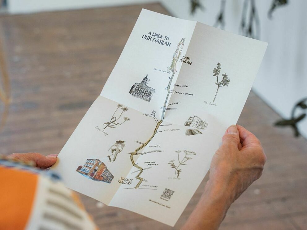A person holding an illustrated A Walk to Our Marian map, showing a route through Nottingham with drawings of plants, landmarks and the Maid Marian sculpture.