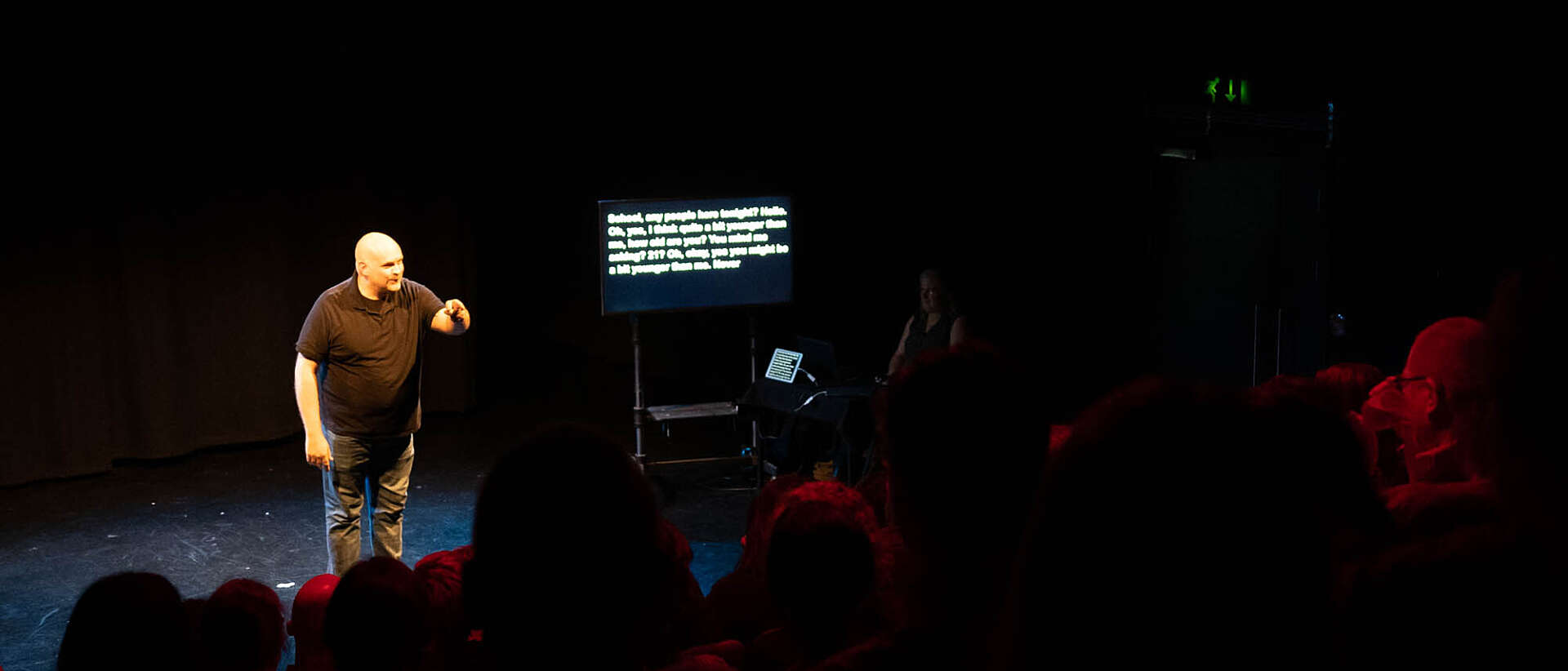 A comedian stands on stage doing stand-up comedy and points towards the audience.