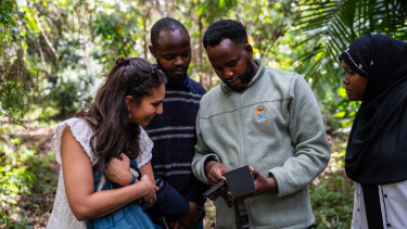 Two men and a woman look closely at a piece of biodiversity monitoring equipment