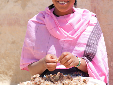 A woman in a pink scarf smiles at the camera as she sorts frankincense in a bowl