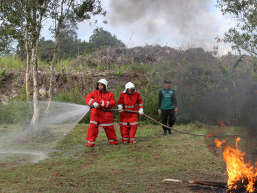Three men in firefighter uniforms using a hose to put out a fire in a clearing in a forest