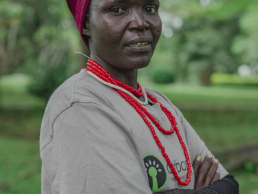 A woman in a red headscarf stands side-on looking at the camera