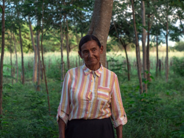 A woman in a striped shirt stands in a wooded area