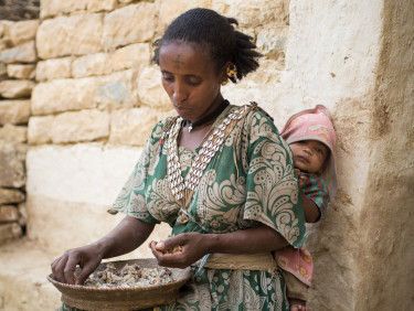 A woman sits sorting a bowl of frankincense with a baby on her back