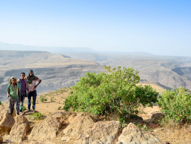 A group of people stand on an outcropping with a dry mountainous landscape behind them