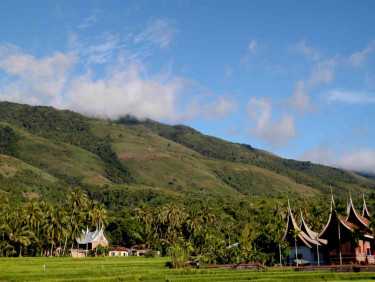 A group of house with pointed roofs in front of wooded hills and a blue sky above