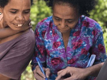 Two women sign a book with plants in the background
