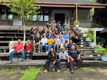 A large group of people sit on the steps in front of a building and its veranda