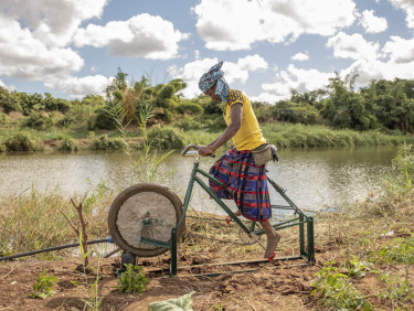 A woman pedals a specially adapted irrigation bike on the banks of a river