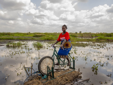 A woman is sitting on a bicycle which is part of an irrigation apparatus in front of a body of water