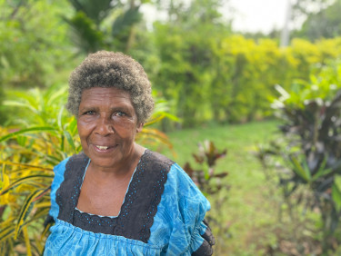 A woman in a blue dress stands with plants in the background