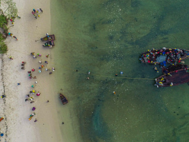 A drone shot of a beach with a group of people and two fishing boats in the water