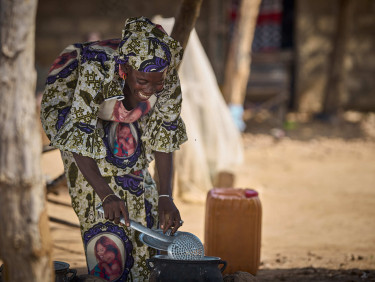 A woman cleans a watering can outside a building