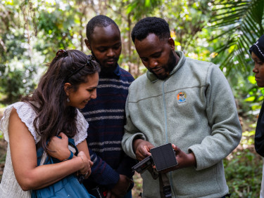 Two men and a woman look closely at a piece of biodiversity monitoring equipment