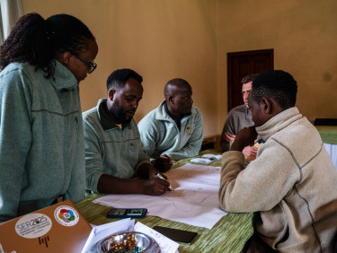 A group of people sit at a table overlooking a large piece of paper