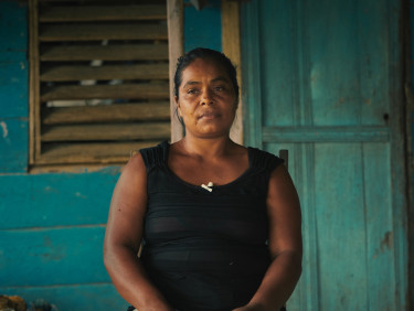 A woman in a black sleeveless top sits outside a wooden building painted blue