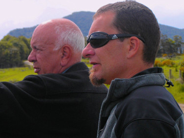 Two men stand in profile, with a mountain in the background