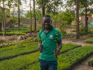 A man in a green polo shirt holding a seedling in front of a tree nursery