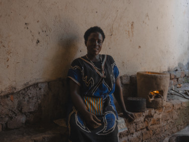 A woman sitting inside a building with a cookstove on the bench next to her
