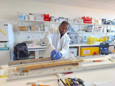 A man in a white coat stands in a lab analysing a soil sample