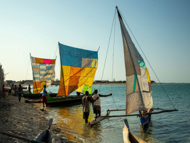 Small boats with colourful patchwork sails on the edge of the beach with some people