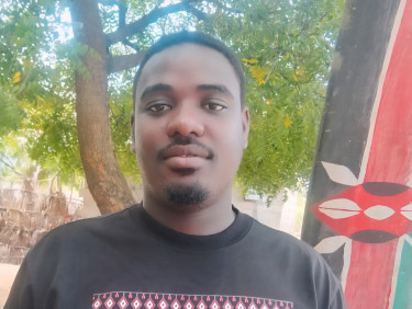 A man in a black t-shirt stands in front of a traditional shield