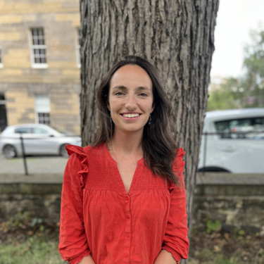 A woman in a red top is smiling in front of a tree