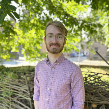 A man in a pink shirt stands in a park