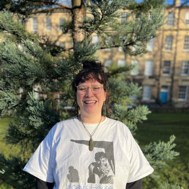 A woman in a white t-shirt stands smiling in front of a tree