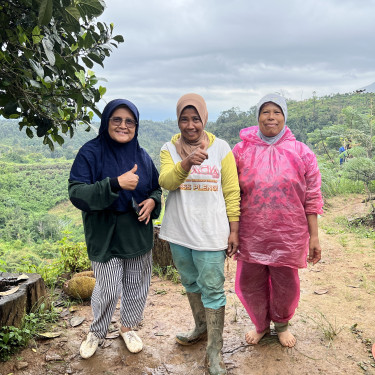 Three ladies stand alongside one another on a muddy rural path