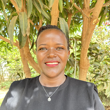 A woman in a grey top stands smiling in front of a tree