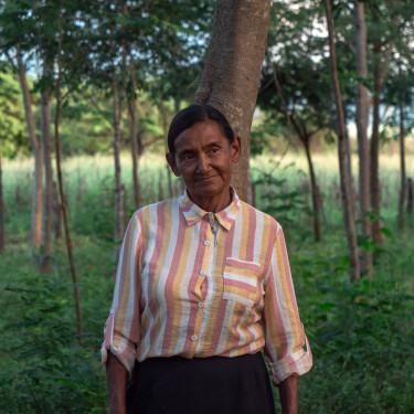 A woman in a striped shirt stands in a wooded area