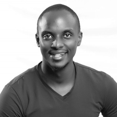 A man in a black t-shirt smiling in front of a white background in greyscale