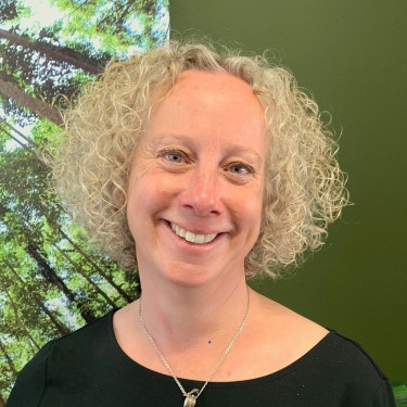 A woman in a black top stands smiling in front of a green wall