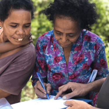 Two women sign a book with plants in the background