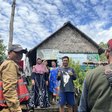 A group of smiling men and women gather on the decking in front of a rural research centre