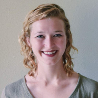 A woman in a grey t-shirt smiles in front of an off-white background