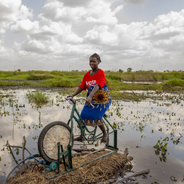 A woman is sitting on a bicycle which is part of an irrigation apparatus in front of a body of water