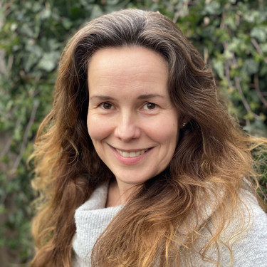 A woman in a white turtleneck smiles in front of ivy
