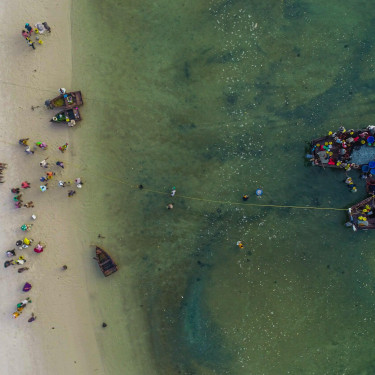 A drone shot of a beach with a group of people and two fishing boats in the water