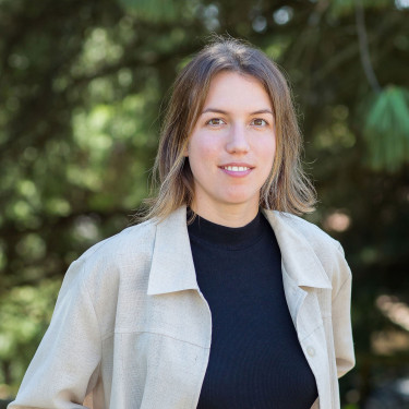 A woman in a white overshirt stands in a forested area