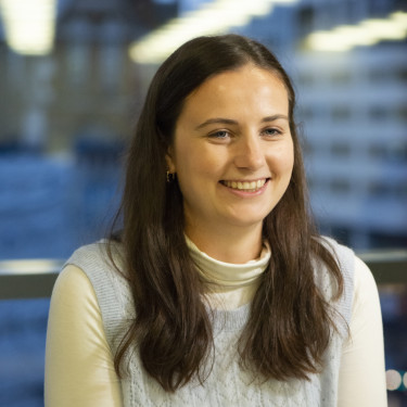 A woman in a white top sits smiling in front of a blue background